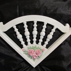 May include: White wooden fan-shaped wall decor with a raised design of a chair back and pink roses.