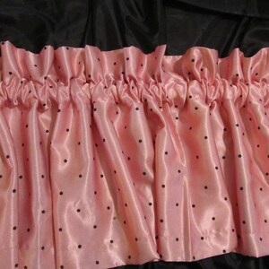 May include: Pink satin valance with black polka dots. The valance is gathered and has a ruffled edge.