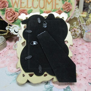 May include: Gold-colored ornate picture frame with a black velvet backing. The frame has a decorative design with floral motifs.