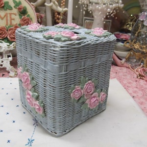May include: A light blue wicker tissue box cover with pink roses and green leaves. The cover is square and has a woven design.