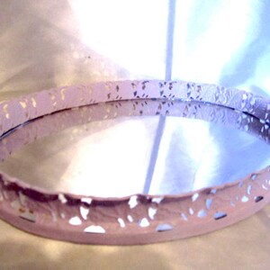 Pu&ograve; includere: Un vassoio ovale bianco con un bordo decorativo a pizzo. Il vassoio ha una superficie a specchio.
