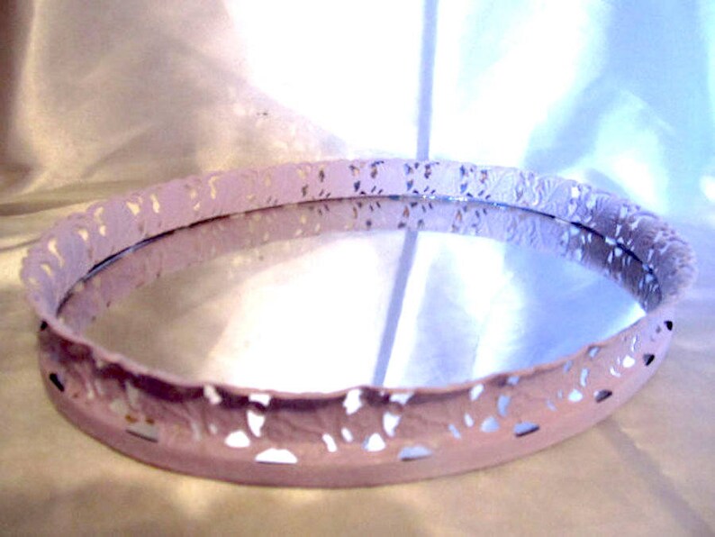 Pu&ograve; includere: Un vassoio ovale bianco con un bordo decorativo a pizzo. Il vassoio ha una superficie a specchio.