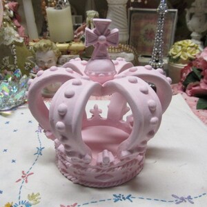 May include: A pink ceramic crown with a cross on top. The crown has a raised design of dots and is perfect for a princess.