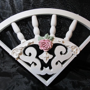 May include: White wooden headboard with a decorative fan shape and a pink rose in the center.
