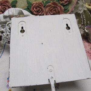 May include: White wooden wall-mounted shelf with two keyhole slots on the back. The shelf has a white painted finish and is ready to be hung.