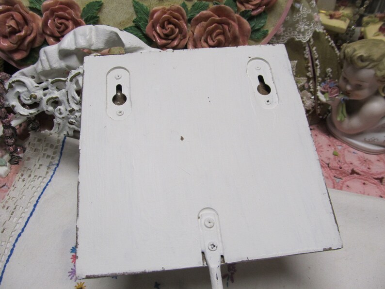 May include: White wooden wall-mounted shelf with two keyhole slots on the back. The shelf has a white painted finish and is ready to be hung.