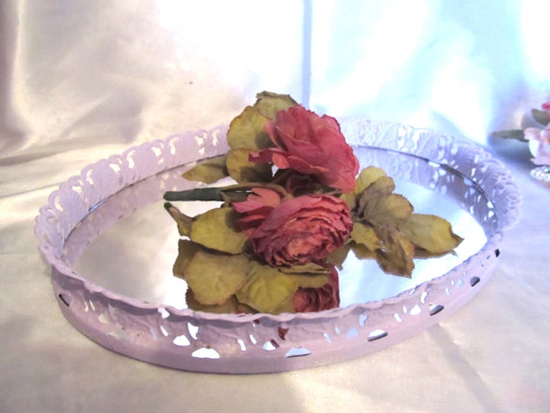 Pu&ograve; includere: Un vassoio ovale di colore lavanda con un bordo decorativo a pizzo. Il vassoio ha una superficie a specchio ed &egrave; decorato con un bouquet di rose rosa.