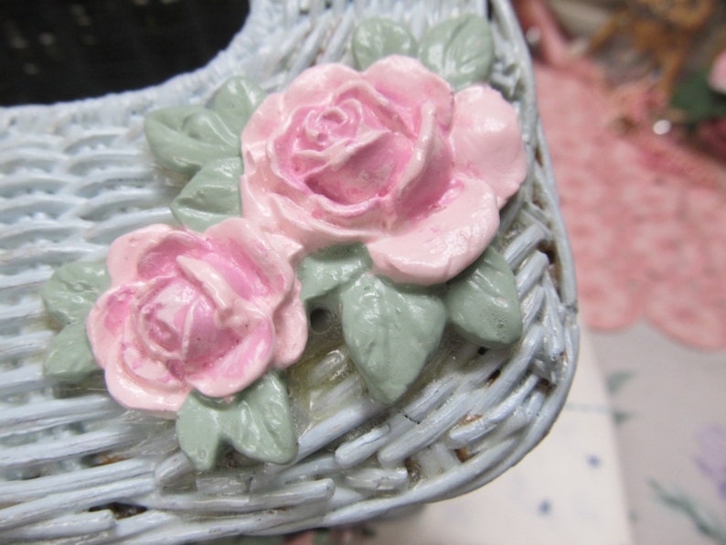 May include: A light blue wicker tissue box cover with two pink roses and green leaves.