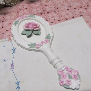 May include: White hand mirror with a raised pink rose design and a white handle with pink roses.
