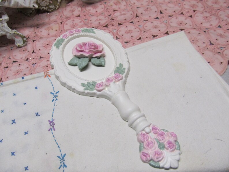 May include: White hand mirror with a raised pink rose design and a white handle with pink roses.