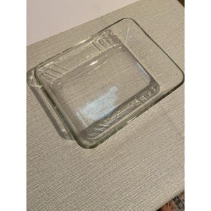 May include: A clear, rectangular glass baking dish with rounded corners and smooth, transparent walls. The dish features a flat bottom and slightly flared sides, providing a simple, functional design for kitchen use and food preparation.