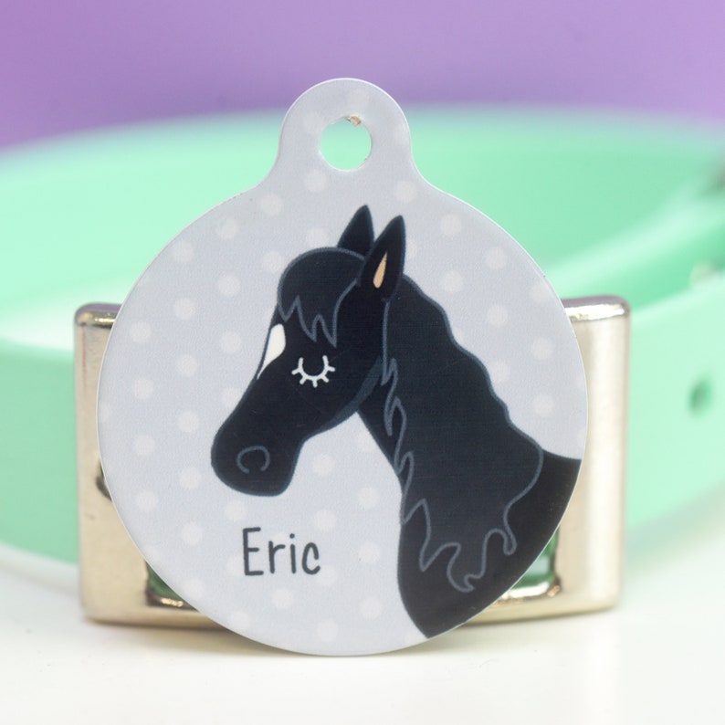 May include: A round, gray pet ID tag with a black and white horse illustration. The tag has a hole for a ring and the name "Eric" printed on it.