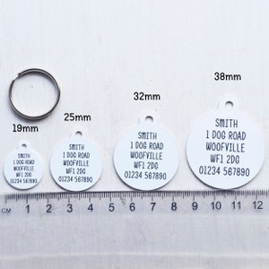 May include: A set of four white, circular pet ID tags with black text, ranging from 0.75 inches to 1.5 inches in diameter. Each tag includes the name "SMITH", an address, and a phone number. A silver metal ring is also included.