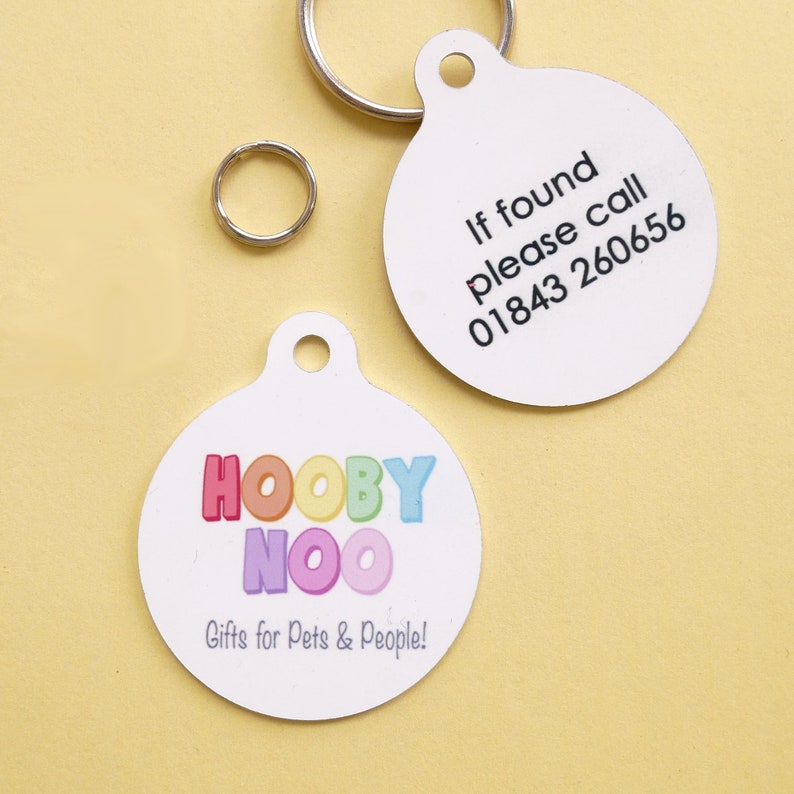 May include: Two white, round pet ID tags with a silver split ring and a smaller ring. One tag has the text "If found please call 01843 260656". The other tag has the text "HOOBY NOO Gifts for Pets & People!" in colorful letters.