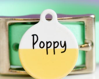 May include: A round white and yellow dog tag with the name "Poppy" written in black.