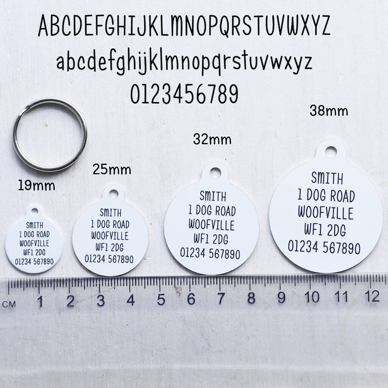 May include: Four white round dog tags with black text. The tags are 1.9 inches, 2.5 inches, 3.2 inches, and 3.8 inches in diameter. The text on the tags reads "SMITH 1 DOG ROAD WOOFVILLE WF1 2DG 01234 567890".