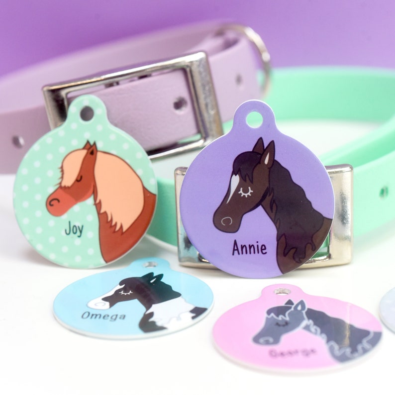 May include: Five colorful round dog tags with horse illustrations and names. The tags are Joy, Annie, Omega, Cassie, and a fifth tag with an unreadable name.