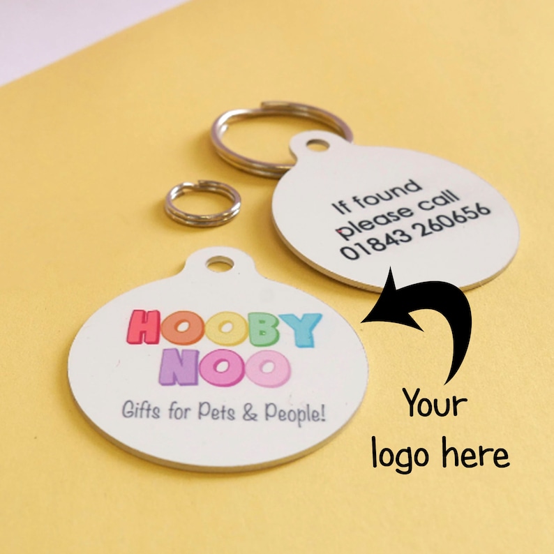 May include: White, round pet tag with the text "HOOBY NOO Gifts for Pets & People!" in colorful letters. Another tag has the text "If found please call 01843 260656". Includes a metal ring for attachment. The background is yellow.