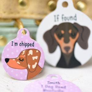 May include: Pet ID tags with dachshund illustrations. One tag is light purple with white polka dots and the text "I'm chipped". Another tag is white with a dachshund face and the text "If found". A third tag is light purple with the name "Smith".
