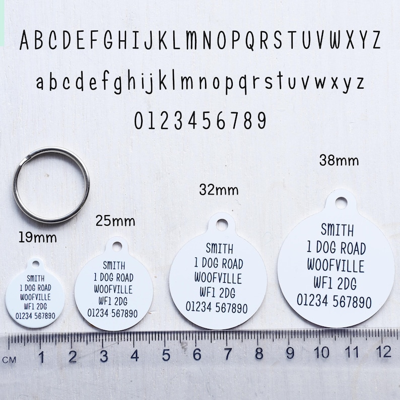May include: White pet ID tags with black text, available in various sizes: 19mm, 25mm, 32mm, and 38mm. Each tag includes the name "SMITH", address, and phone number. A silver metal ring is also shown.
