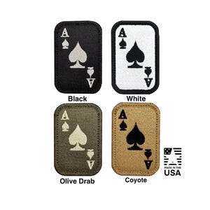Pode incluir: Quatro emblemas retangulares bordados com um design de carta de Ás de Espadas. Os emblemas vêm nas cores preto, branco, verde-oliva e coiote com fio contrastante para a letra A e o símbolo de espadas. O texto diz Black, White, Olive Drab, Coyote e MADE IN THE USA.