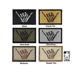 Puede incluir: Seis parches rectangulares bordados con una mano esquelética haciendo un gesto shaka. Los colores incluyen negro, coyote tan, verde oliva, plata/gris, multicam y desert tan. Cada parche tiene un borde y el texto Made in the USA.