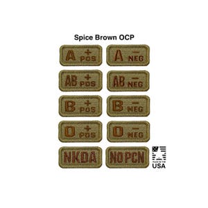 May include: A collection of ten rectangular Spice Brown OCP blood type and medical alert patches. The patches feature embroidered brown text on a tan background, including A, AB, B, O, POS, NEG, NKDA, and NOPCN. The text Spice Brown OCP is centered above.