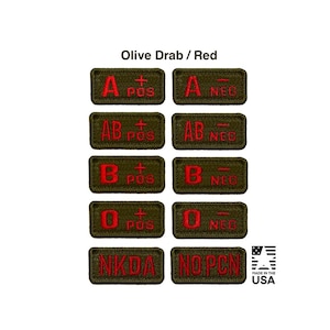 May include: A collection of rectangular olive drab embroidered patches featuring red text for blood types A, AB, B, and O, with positive or negative indicators, plus NKDA and NOPCN labels. The text Olive Drab / Red appears at the top, with a Made in the USA logo.