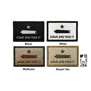 Puede incluir: Cuatro parches rectangulares bordados que presentan un cañón, una estrella solitaria y el texto "COME AND TAKE IT". Los parches están disponibles en colores negro, blanco, multicam y tostado desierto. Un logotipo "MADE IN THE USA" es visible en la esquina.
