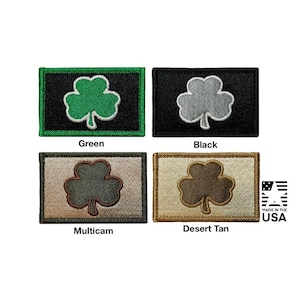May include: Four rectangular embroidered patches featuring a shamrock design. The top left is green on black, top right is grey on black, bottom left is dark green on multicam, and bottom right is brown on desert tan. Text reads Made in the USA.