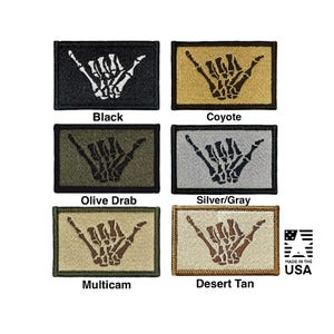 Può includere: Sei toppe rettangolari ricamate raffiguranti una mano scheletrica che fa un gesto shaka. I colori includono nero, coyote, verde oliva, argento/grigio, multicam e beige deserto. Ogni toppa è etichettata con il nome del colore e un logo Made in the USA.
