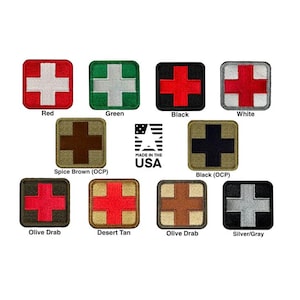 May include: A collection of twelve square embroidered patches, each featuring a central cross design in various colour combinations including red, white, green, black, spice brown, olive drab, and desert tan. The text MADE IN THE USA is visible.