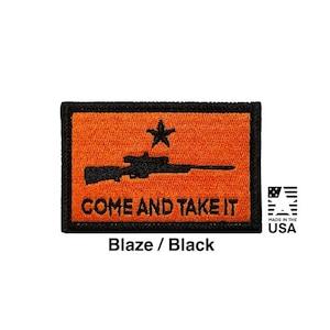 Könnte beinhalten: Ein rechteckiger bestickter Aufnäher mit leuchtend orangefarbenem Hintergrund und schwarzem Rand. Das Design zeigt die Silhouette eines schwarzen Gewehrs, einen schwarzen Stern darüber und den schwarzen Text "COME AND TAKE IT".