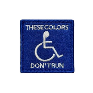 Puede incluir: Un parche cuadrado bordado en azul con un símbolo blanco de accesibilidad para sillas de ruedas en el centro. El texto "THESE COLORS" está bordado en blanco sobre el símbolo, y el texto "DON'T RUN" está bordado en blanco debajo.