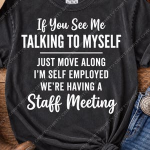 May include: A black short-sleeved t-shirt with white text that reads: If You See Me TALKING TO MYSELF JUST MOVE ALONG I'M SELF EMPLOYED WE'RE HAVING A Staff Meeting. The shirt features a crew neckline and a vintage-style washed fabric finish.