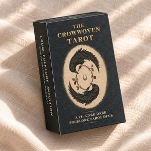 Pode incluir: Uma caixa retangular preta para baralho de tarot com o título The Crowwoven Tarot em letras douradas. A frente apresenta uma ilustração oval de dois corvos circulando um ovo central e vinhas espinhosas. O texto lateral diz Crow. Folklore. Intuition.