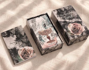Puede incluir: Una baraja de cartas The Textured Tarot con un patrón oscuro y texturizado de flores y hojas con una rosa rosada. El set incluye una caja de almacenamiento a juego, una tapa y una carta que muestra el As de Copas con un cáliz.