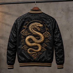 May include: A black satin varsity jacket featuring a large, detailed gold-toned embroidery of a coiled snake surrounded by stylized clouds on the back. The jacket has ribbed black and gold striped cuffs, collar, and hem, with quilted shoulder panels.