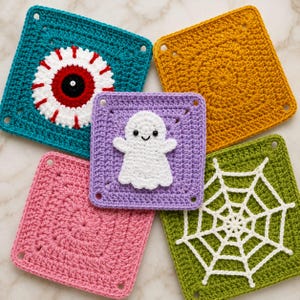 May include: Five square crochet patches featuring Halloween designs. One teal patch has a large red and white eyeball. One mustard yellow patch is plain. One lavender patch features a white ghost. One pink patch is plain. One green patch has a white spiderweb.