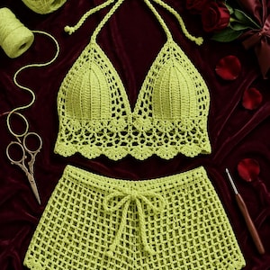 Puede incluir: Un conjunto de dos piezas de ganchillo en color verde lima que consta de un top halter y pantalones cortos. El top halter presenta un diseño de copas triangulares con un dobladillo festoneado. Los pantalones tienen un patrón de rejilla.