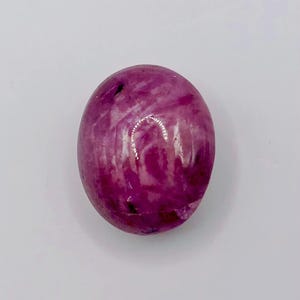 Könnte beinhalten: Ein glatter, polierter, oval geformter Edelstein mit einer leuchtenden Farbpalette in Magenta und Dunkelrosa. Die Oberfläche weist natürliche weiße Marmorierungsmuster und kleine dunkle Einschlüsse auf, die eine Textur erzeugen.