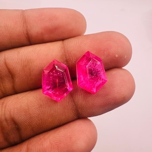 May include: Two loose, faceted, shield-shaped gemstones with a vibrant, translucent hot pink colour. Each stone features a geometric cut with multiple flat surfaces that reflect light, creating a bright, saturated appearance.