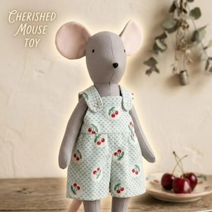 May include: A grey plush mouse toy with large ears and a black nose, wearing light green dungarees featuring a white polka dot pattern and a red cherry print. The text "CHERISHED MOUSE TOY" is visible in the upper left corner of the image.