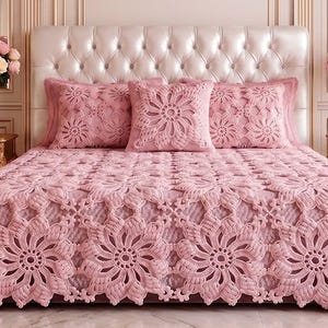 Pode incluir: Uma colcha de crochê rosa claro e almofadas quadradas combinando com um motivo floral repetitivo. A roupa de cama é exibida em uma cabeceira branca capitonê, ladeada por duas mesas de cabeceira douradas com vasos de rosas rosas e brancas.
