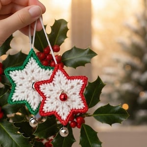 May include: Two star-shaped crochet ornaments featuring white centers with red and green borders. Each star has a small metallic bell attached to the bottom point and a white string loop at the top for hanging. The ornaments are crafted with yarn.