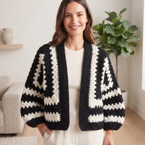 Op de afbeelding: Een zwart-wit gehaakt vest met een geometrisch granny square patroon, een open voorzijde, lange mouwen en een relaxte pasvorm. Het kledingstuk is gemaakt met afwisselende blokken van effen zwart en wit garen in een gestructureerde steek.