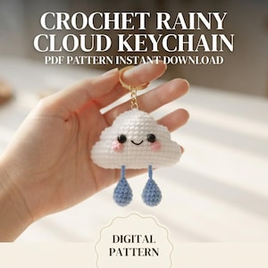 Può includere: Un portachiavi a forma di nuvola bianca all'uncinetto con un viso sorridente, guance rosa e due gocce di pioggia blu pendenti attaccate a un anello di metallo dorato. Il testo CROCHET RAINY CLOUD KEYCHAIN PDF PATTERN INSTANT DOWNLOAD e DIGITAL PATTERN è visibile.