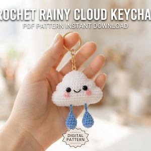 Könnte beinhalten: Ein weißer Häkel-Wolken-Schlüsselanhänger mit lächelndem Gesicht, rosa Wangen und zwei baumelnden blauen Häkel-Regentropfen an einem goldfarbenen Metallring. Der Text CROCHET RAINY CLOUD KEYCHAIN PDF PATTERN INSTANT DOWNLOAD und DIGITAL PATTERN ist sichtbar.