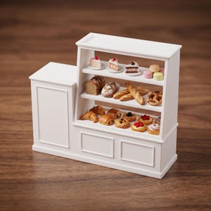 Könnte beinhalten: Eine weiße Miniatur-Bäckereitheke mit drei Regalen, die mit winzigen Lebensmitteln bestückt sind. Die Regale enthalten kleine Kuchen, Macarons, Brotlaibe, Baguettes, eine Brezel, Croissants, Plundergebäck und mit Früchten belegte Törtchen.