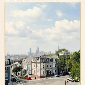 May include: A print featuring the text SOUTHIE BOSTON at the top and The city collection at the bottom. The image shows a street scene with multi-story residential buildings, a road intersection, and a distant city skyline under a cloudy sky.